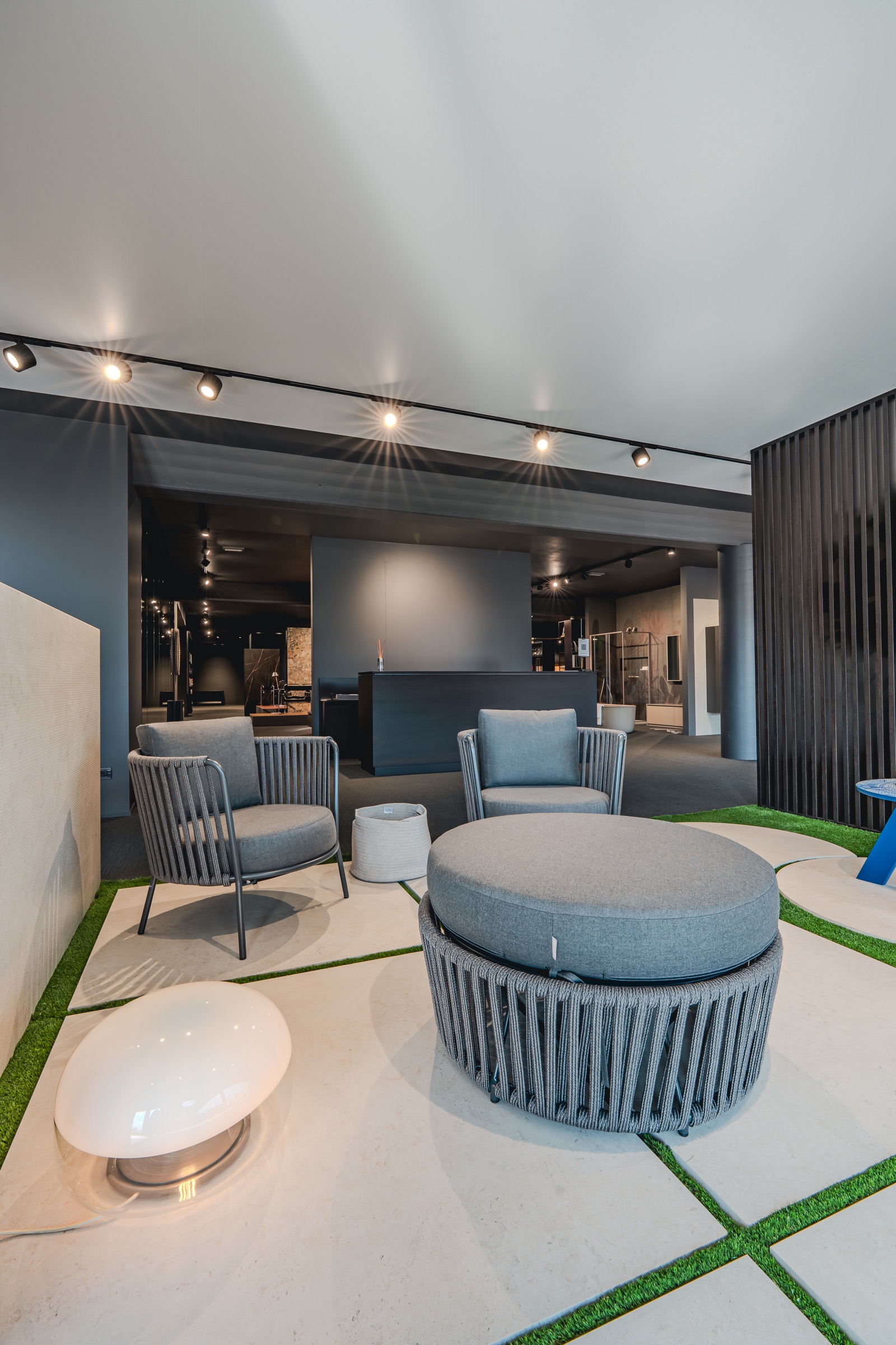 Area lounge dello showroom con sedute grigie e lampada in vetro